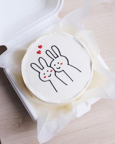 a cake with two rabbits on it sitting in a box next to a knife and fork