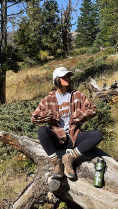 a woman sitting on top of a fallen tree in the woods next to a cup