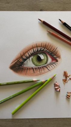 pencils and crayons are laying next to an eye with green eyeshade