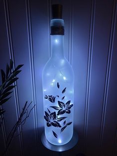 a lighted bottle with flowers on it next to a potted plant