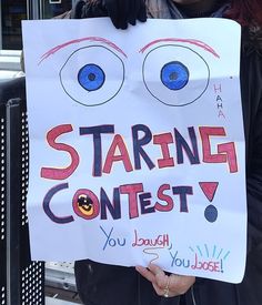 a woman holding up a sign that reads starting contest you laugh with eyes on it