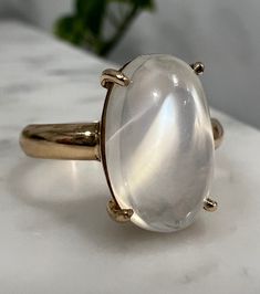 Offered here is a seriously stunning vintage  moonstone set in 18k yellow gold.  The ring boasts a magnificent 5.4 Ct oval moonstone with desirable adularescence effects with strong white hues and some blue flashes when the light hits one end. In regular terms that means light will make the top of the stone have the appearance of a moving floating, cloud-like, white light inside the gem, similar to moonlight dancing on still water.  Generally, the more transparent and colorless the body and more blue the adularescence, the higher the moonstone value. This stone is held in a 4 prong setting in 18k gold and the moonstone has a known weight of 5.4 carats as it was newly re-set to tighten the prongs. The moonstone looks magnificent catching the light and crowning the finger. It is approx a siz Luxury Classic Moonstone Ring, Elegant Domed Moonstone Ring, White Oval Moonstone Ring With Large Stone, Unique Moonstone Ring With Large Stone, Elegant Domed Moonstone Gemstone Ring, Yellow Gold Oval Cabochon Moonstone Ring For Anniversary, Classic Oval Moonstone Ring, Modern Oval Cabochon Moonstone Ring For Formal Occasions, Classic White Moonstone Ring