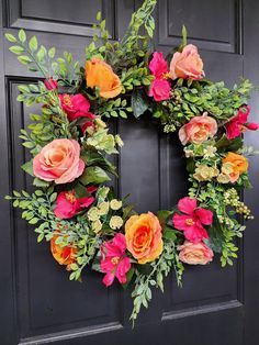 a wreath with flowers and greenery hanging on the front door to decorate it for someone's special occasion