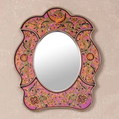 an ornate mirror with pink and gold designs on the front, hanging on a wall