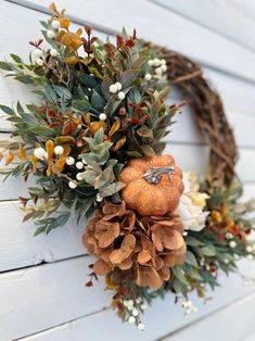 a wreath is hanging on the side of a white building with flowers and leaves around it