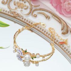 Exquisitely romantic, this gold-plated bracelet showcases a lush garland of wild roses, accented with shimmering freshwater pearls and delicate purple flowers. Designed with a purple floral design captures the natural elegance of the wild rose, complemented by verdant leaves. This captivating accessory lends an enchanting, feminine touch, elevating any outfit with its harmonious blend of gilded metal, lustrous pearls, and vibrant botanicals. DETAILS Plating: 18K Gold Materials: 18K Gold on Brass Gold Pearl Flower Bracelets, Gold Flower Pearl Bracelet For Wedding, Dainty Gold Flower Pearl Bracelet, Rose Bracelet, Wild Rose, Enamel Flower, Gold Plated Bracelets, Flower Bracelet, Wild Roses