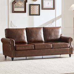 a brown leather couch sitting on top of a carpeted floor next to framed pictures