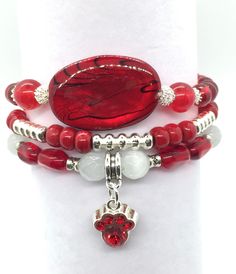 Ruby red makes me think of the hot summer days of July. It's so fitting that the ruby is July's  birthstone. This 3 bracelet set has a large shell focal, flanked by red jade, red glass beads, white cat eye, silver tone accents and a ruby red paw charm. Your bracelets will arrive in a jewelry box, perfect for gifting or keeping. **Please note** I have used strong 1 mm elastic and I use a triple tie on my bracelets to be sure they are secure. However, repeated stretching over your hand will eventu Red Beaded Bracelets With Natural Stones As Gift, Red Ruby Bracelets As Gift, Red Gemstone Beads Crystal Bracelet Gift, Red Natural Stones Bracelets For Gift, Red Gemstone Beaded Bracelets For Jewelry Making, Red Wrap Bracelet With Round Beads For Gift, Hand Wrapped Round Red Jewelry, Red Ruby Bracelet As Gift, Hand Wrapped Red Round Jewelry