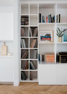 a white bookcase filled with lots of books on top of a hard wood floor