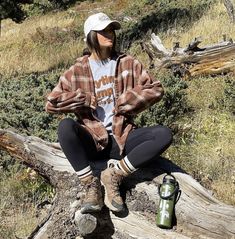 a woman sitting on top of a tree log next to a backpack and water bottle