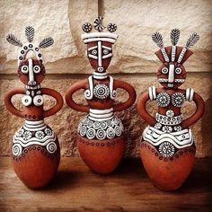 three clay sculptures sitting on top of a wooden table next to a stone block wall