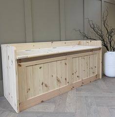 a wooden bench sitting on top of a hard wood floor next to a white vase