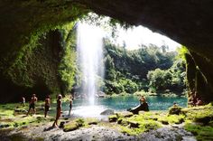 people are sitting on the rocks near a waterfall and swimming in the water while others stand around