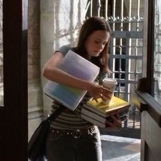 a girl is holding books and looking down at her cell phone while standing in front of an open door