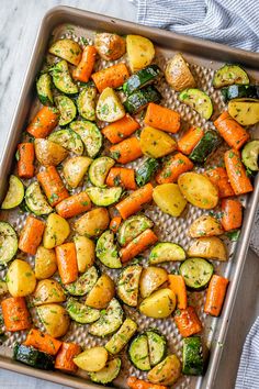 a pan filled with roasted vegetables on top of a white table cloth next to a blue towel