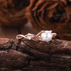 a white pearl ring sitting on top of a piece of wood with flowers in the background