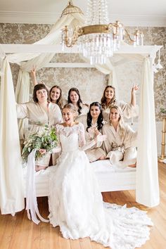 a bride and her bridal party posing for a photo on the bed in their wedding suite