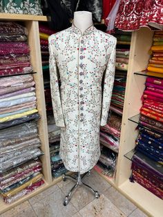 Men's Ivory sherwani with all-over blue and red thread embroidery ( French knot stitch with zardozi work). This sherwani is an easy to match with most lehengas Comes with Ivory churidars. Crafted with a collar neckline, full sleeves, and front button closure. Occasion: Can be worn to events like Wedding WASH CARE INSTRUCTIONS - Please Dry clean only when it is applicable. Slight color variation is possible due to digital photography. Semi-stitched Floral Embroidered Sherwani For Eid, Bollywood Style Floral Embroidered Sherwani For Eid, Eid Bollywood Sherwani With Floral Embroidery, Diwali Sherwani With Floral Embroidery In Raw Silk, White Sherwani With Floral Embroidery For Diwali, Festive Sherwani With Floral Embroidery For Festivals, Designer Floral Embroidered Traditional Sherwani, Diwali White Sherwani With Floral Embroidery, Semi-stitched Floral Sherwani For Diwali