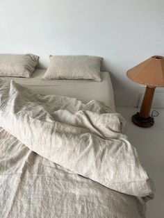 an unmade bed with two pillows and a lamp on the nightstand next to it