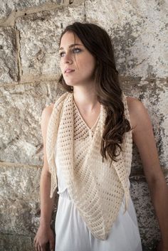 a woman standing in front of a stone wall wearing a crocheted shawl