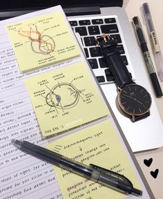 a watch, pen and notebooks on a desk next to a laptop with notes