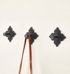 two black scallop hooks on a white wall with a brown leather strap hanging from it