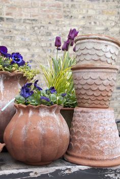 three clay vases with flowers in them sitting on a table next to a brick wall