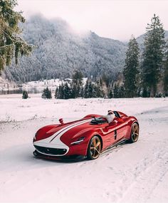 a red sports car driving down a snow covered road in the middle of winter time