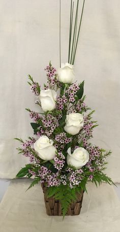 a bouquet of white roses and greenery in a wooden basket on a table top