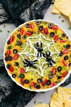 a halloween pizza with black olives, tomatoes and cheese on it next to tortilla chips