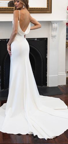 a woman in a white dress standing next to a fireplace with her back turned towards the camera