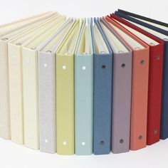 a row of colored binders sitting next to each other on top of a white surface