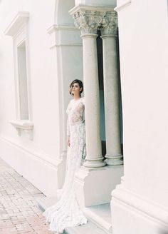 a woman in a white wedding dress standing on the side of a building with columns