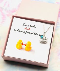 two yellow rubber ducks sitting in a pink box with a necklace on it's neck