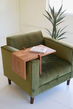 a green chair with a small wooden table on it's back end in front of a potted plant