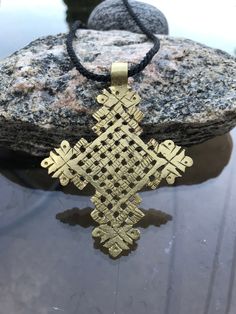 a gold cross pendant sitting on top of a rock