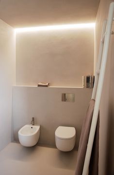 two white toilets sitting next to each other in a bathroom under a light that is on