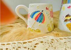 two coffee mugs sitting on top of a table next to each other with an umbrella painted on them