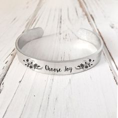 a close up of a metal bracelet on a wooden surface with the words choose joy