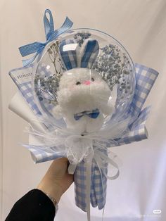 a hand holding a white stuffed animal in a blue and white bow with flowers on it