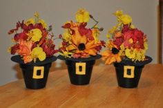 three black vases with yellow and red flowers in them on a wooden table top