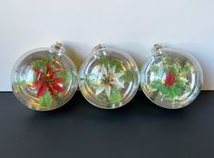 three clear glass vases with red and green flowers in them on a black surface