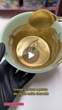 a person in black gloves is pouring liquid into a bowl with a gold spoon on it