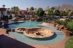 an outdoor swimming pool surrounded by palm trees and rocks with a fire pit in the middle