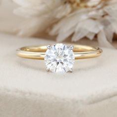 a close up view of a diamond ring on a white cloth with flowers in the background