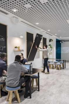 people sitting at desks in an office with chalkboards on the wall and writing on the blackboard