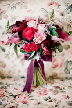 a bouquet of flowers sitting on top of a floral print couch cushion with purple ribbon