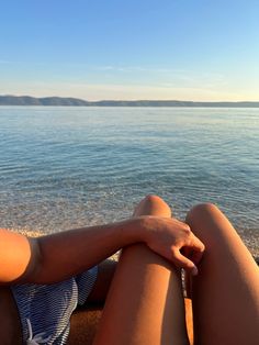 a woman laying on the beach with her legs crossed and looking out at the water