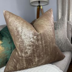 two brown and green pillows sitting on top of a white couch next to a lamp