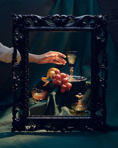 a person holding a wine glass in front of a painting with fruit on the table